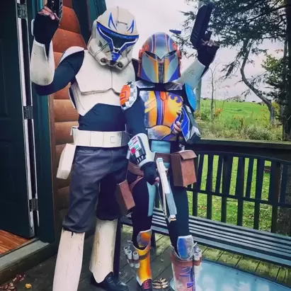 Two Clone Wars cosplayers stand together in full armor, one is wearing a painted Sabine helmet. 